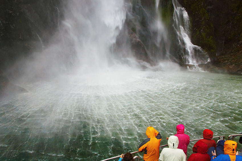 People on the boat near spectacular waterfall, Milford Sound fiord, New Zealand
