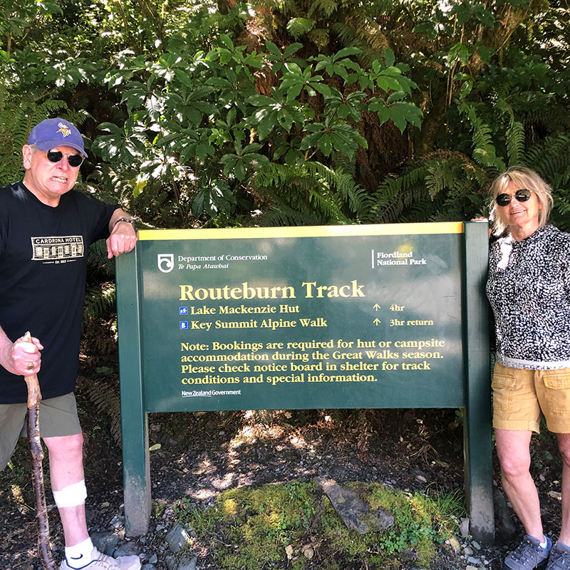 Clients of The Road Trip New Zealand in front of the Routeburn Track sign at Fiordland National Park