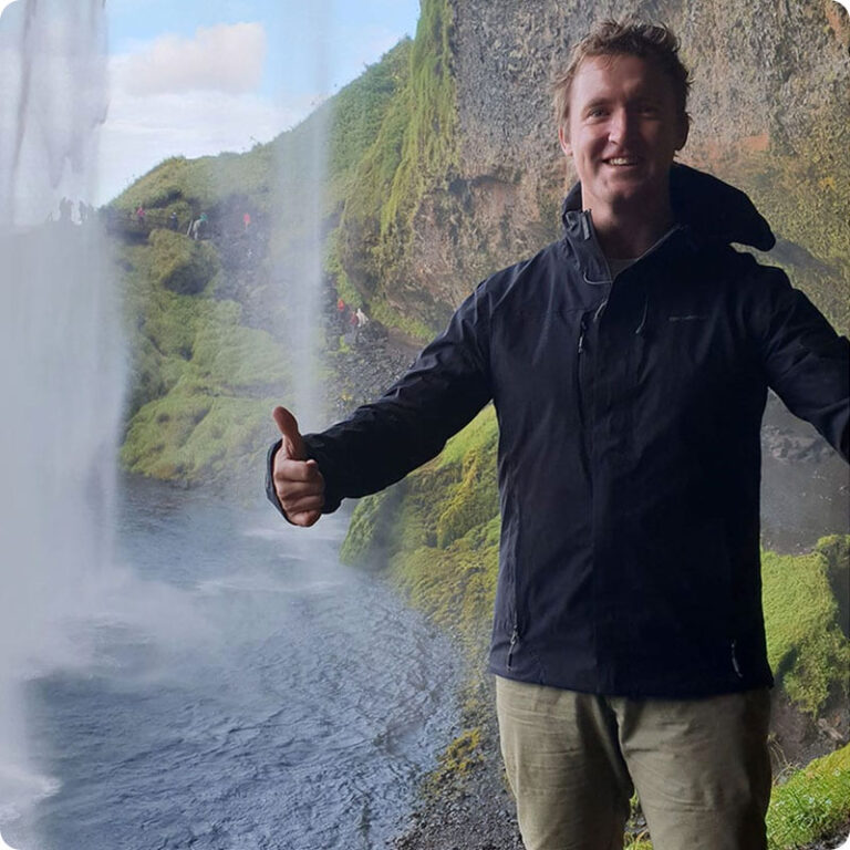 Chris Cameron standing underneath a waterfall in New Zealand