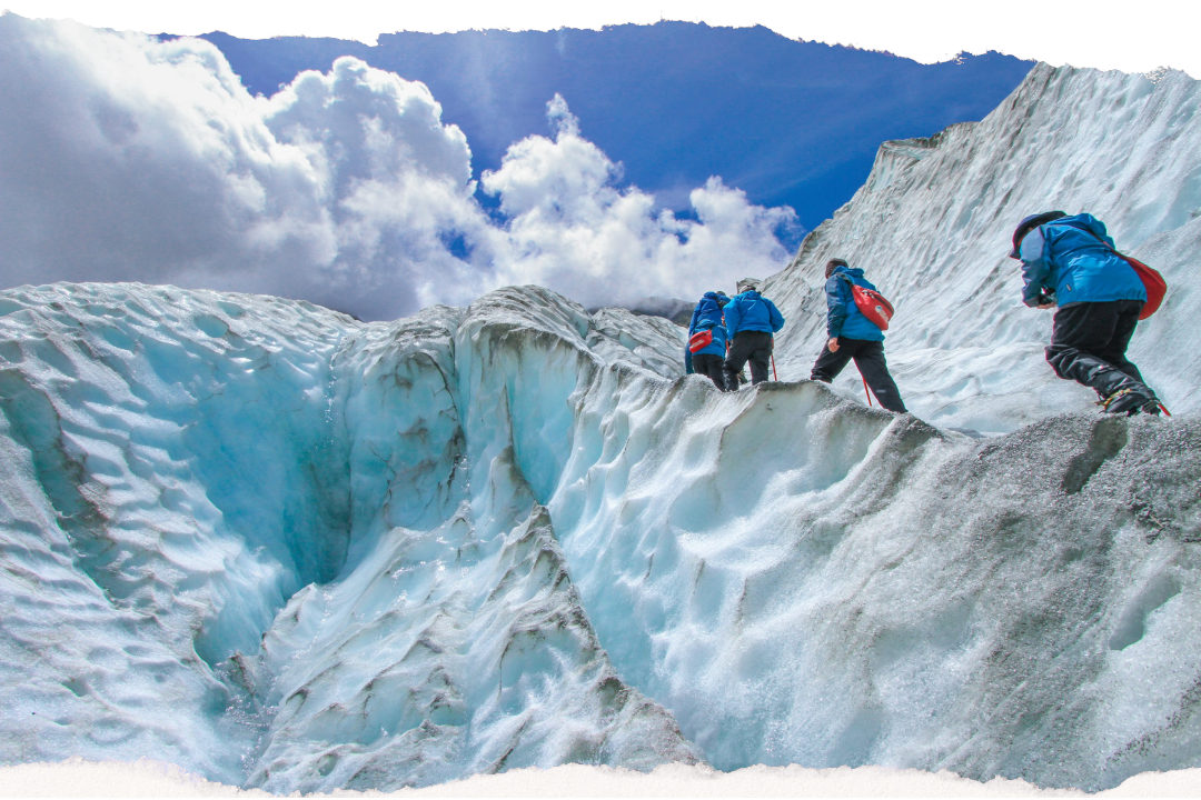 Hikers crossing the ice on Franz Josef Glacier with mountains behind
