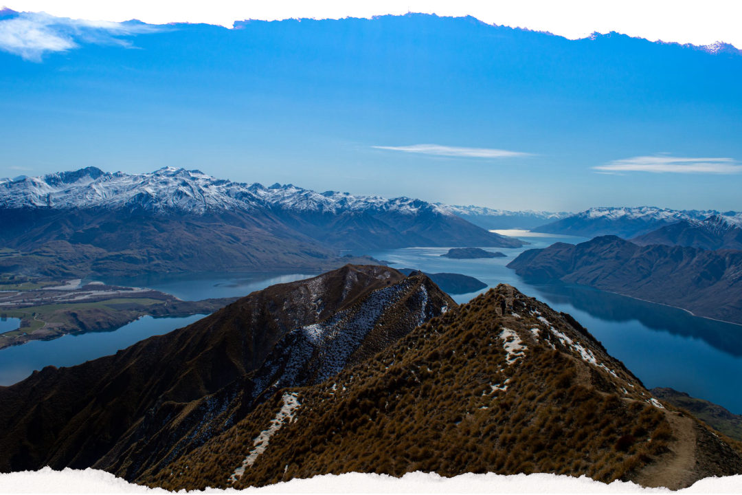 Looking down over Lake Wanaka and the islands sitting in it from a tussock ridge, with the snow-capped Southern Alps beyond